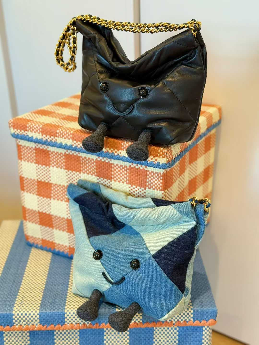 Black handbag with a smiley face design on top of a checkered box, with a blue star-shaped bag below.