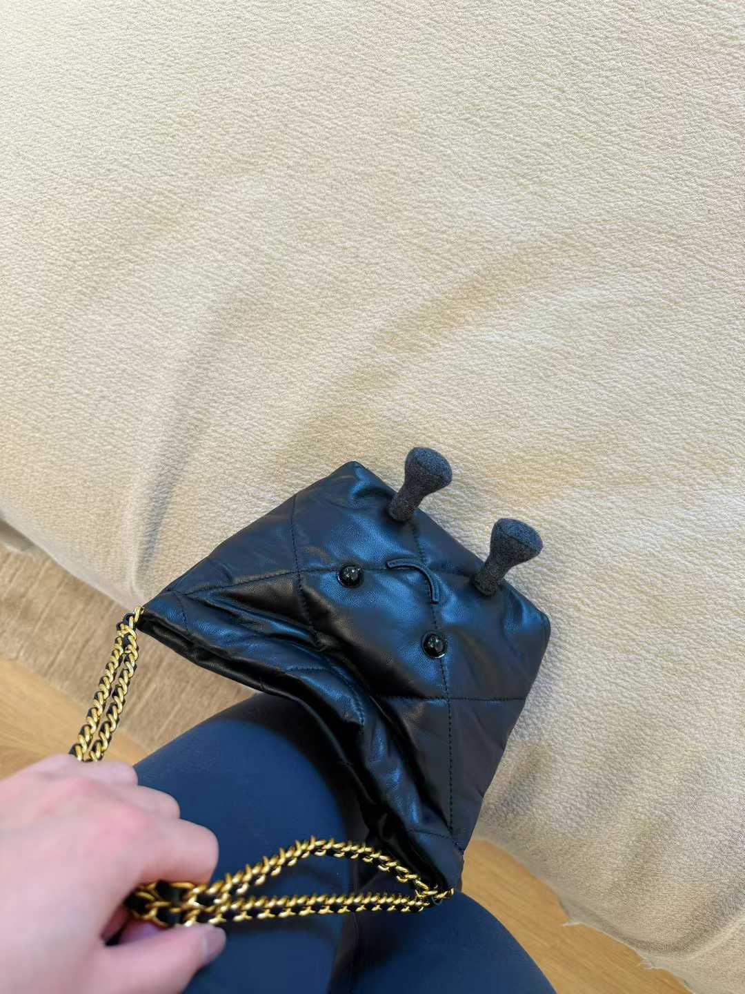 Black leather glove with gold chain held by a hand on a beige surface